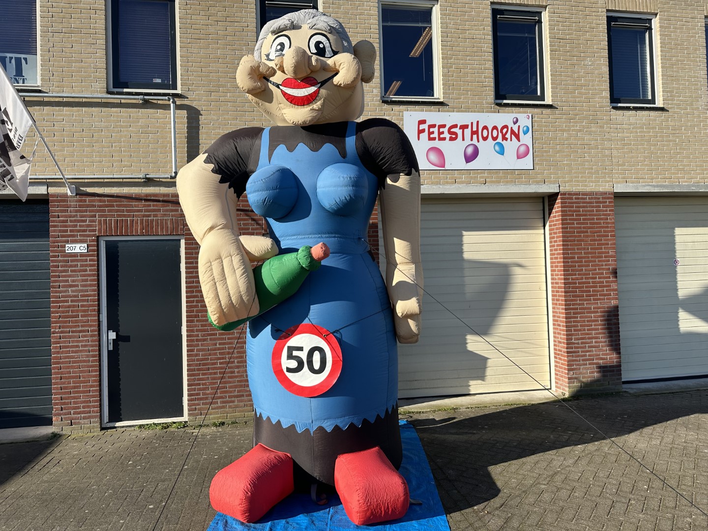 De Sarah Cartoon XL met een wijnfles in de hand. Heeft een hoogte van 4.2 meter. standaard geleverd met leeftijdbanner 50. Er is ook keuze uit 16, 18, 21, 25, 30, 35, 40, 60, 65, Pensioen!!, 67, 70 en 80 jaar.