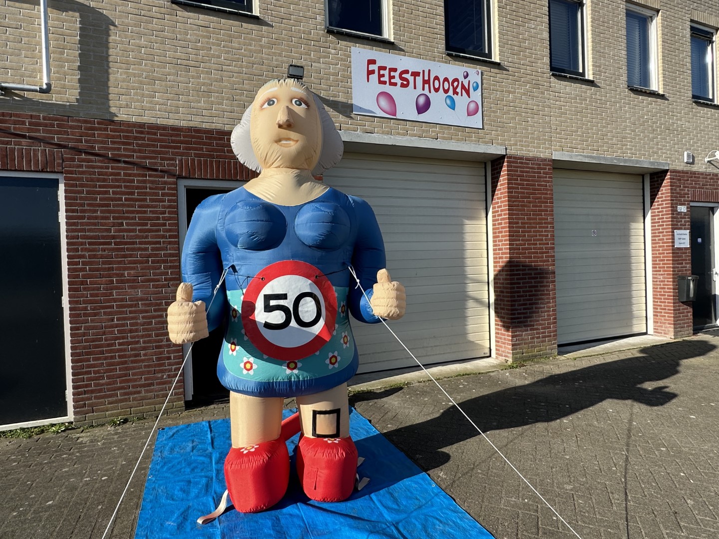 De opblaasbare Sarah L pop van 2,8 meter met duimen omhoog. Geleverd met een verkeersbordbanner naar keuze of een 'pensioen' banner.