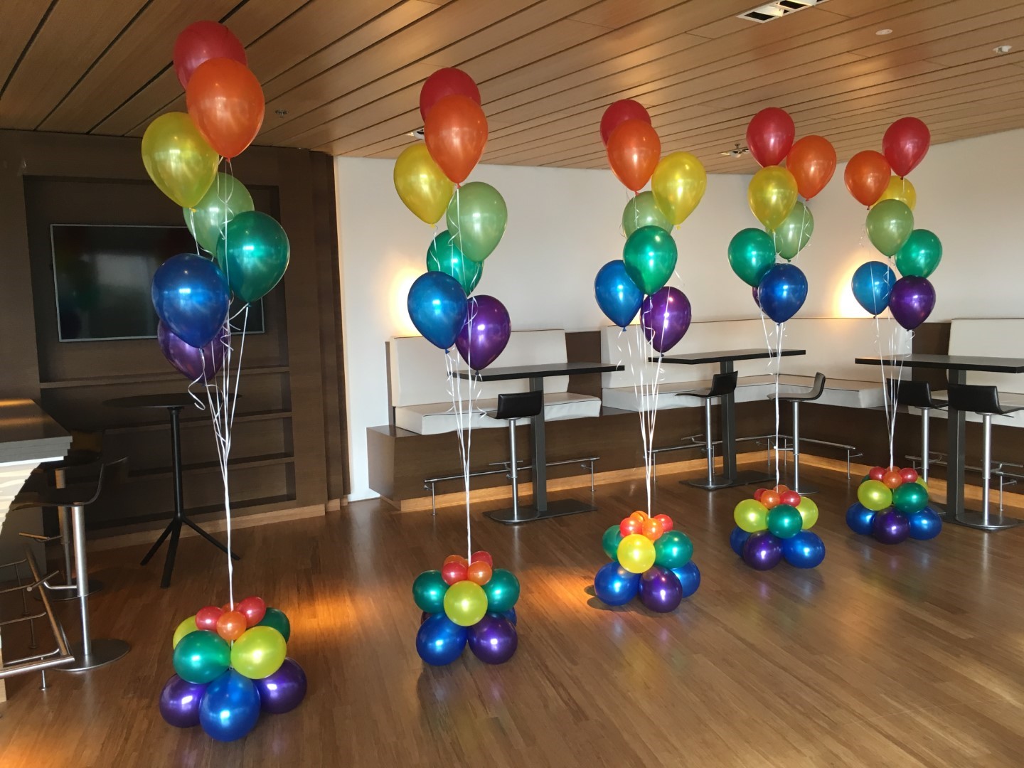 Regenboog boeketten samengesteld in de bekende regenboog kleuren aan lint voorzien van een verzwaard grondcluster van ballonnen.