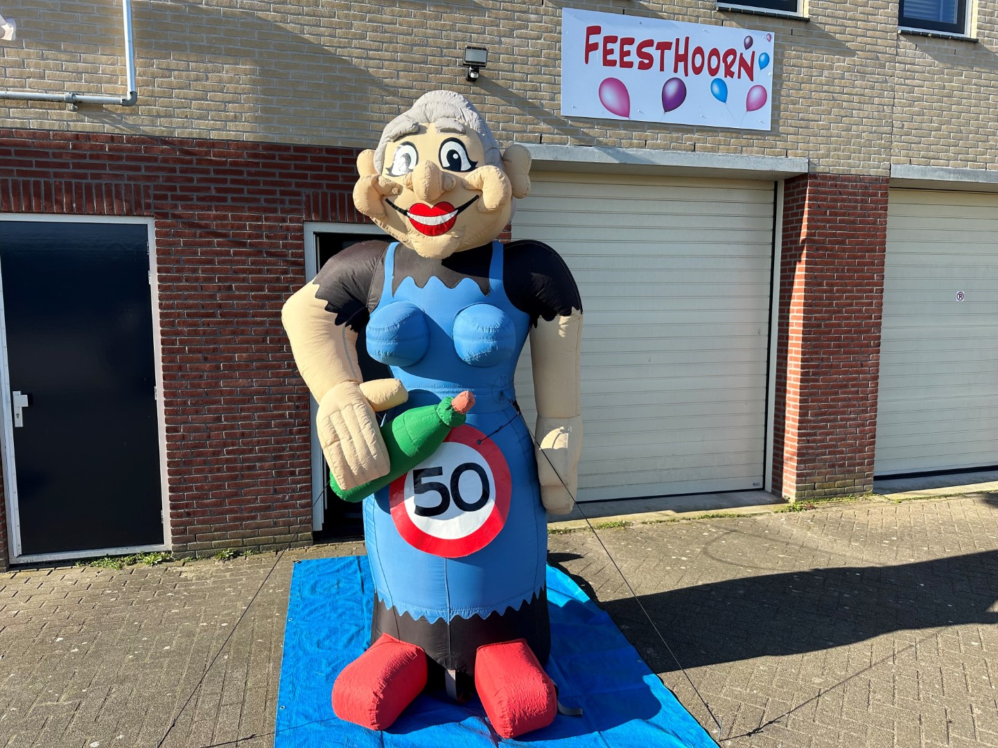 De Sarah Cartoon L met een wijnfles in de hand. Heeft een hoogte van 3.2 meter. Wordt standaard geleverd met een ’50’ verkeersbordbanner. Er is eventueel ook keuze uit een ander getal of een ‘pensioen’ banner.